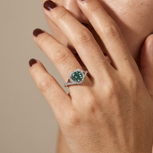 Close-up of a hand with the 1-carat heart moissanite halo ring in platinum-plated sterling silver available in green, yellow, and white with a beige background