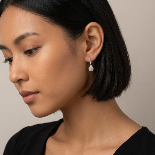 Close-up of a woman wearing moissanite huggie drop earrings in sterling silver, with a neutral background