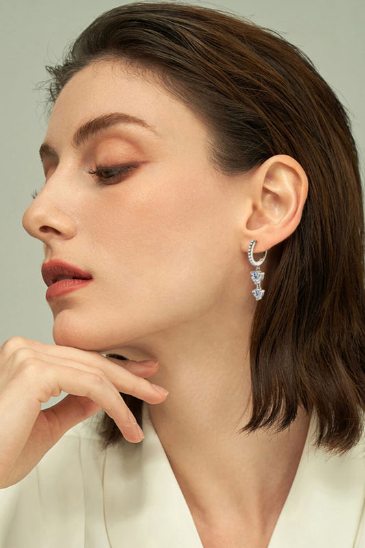 Close-up of a woman wearing 0.5 carat moissanite drop earrings in sterling silver with gold accents, with a neutral background