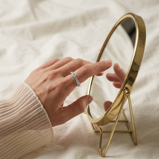 Gold-framed mirror on a white surface with a woman's hand touching it, wearing the Eternyx moissanite hexagon eternity ring in rhodium-plated sterling silver by MerchLuxx