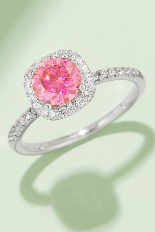 Adorea 1-carat moissanite halo ring in sterling silver by MerchLuxx with a central pink moissanite surrounded by smaller clear stones on a green background.
