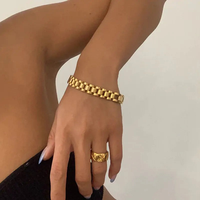 A person's wrist is wearing a Velmora gold link bracelet in 18K PVD plated stainless steel, a luxury adjustable watch link bracelet by MerchLuxx with a ring on the same finger, suggesting elegance and luxury.