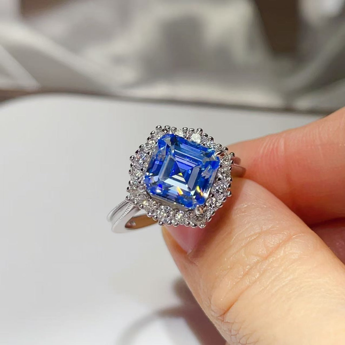 Angled close-up of the Sapphire™ Blue Halo Ring held between fingers