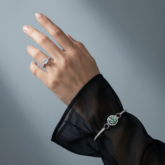 Hand wearing a 1.21 carat princess cut moissanite ring with pavé side stones in platinum-plated sterling silver and a matching bracelet on a gray background