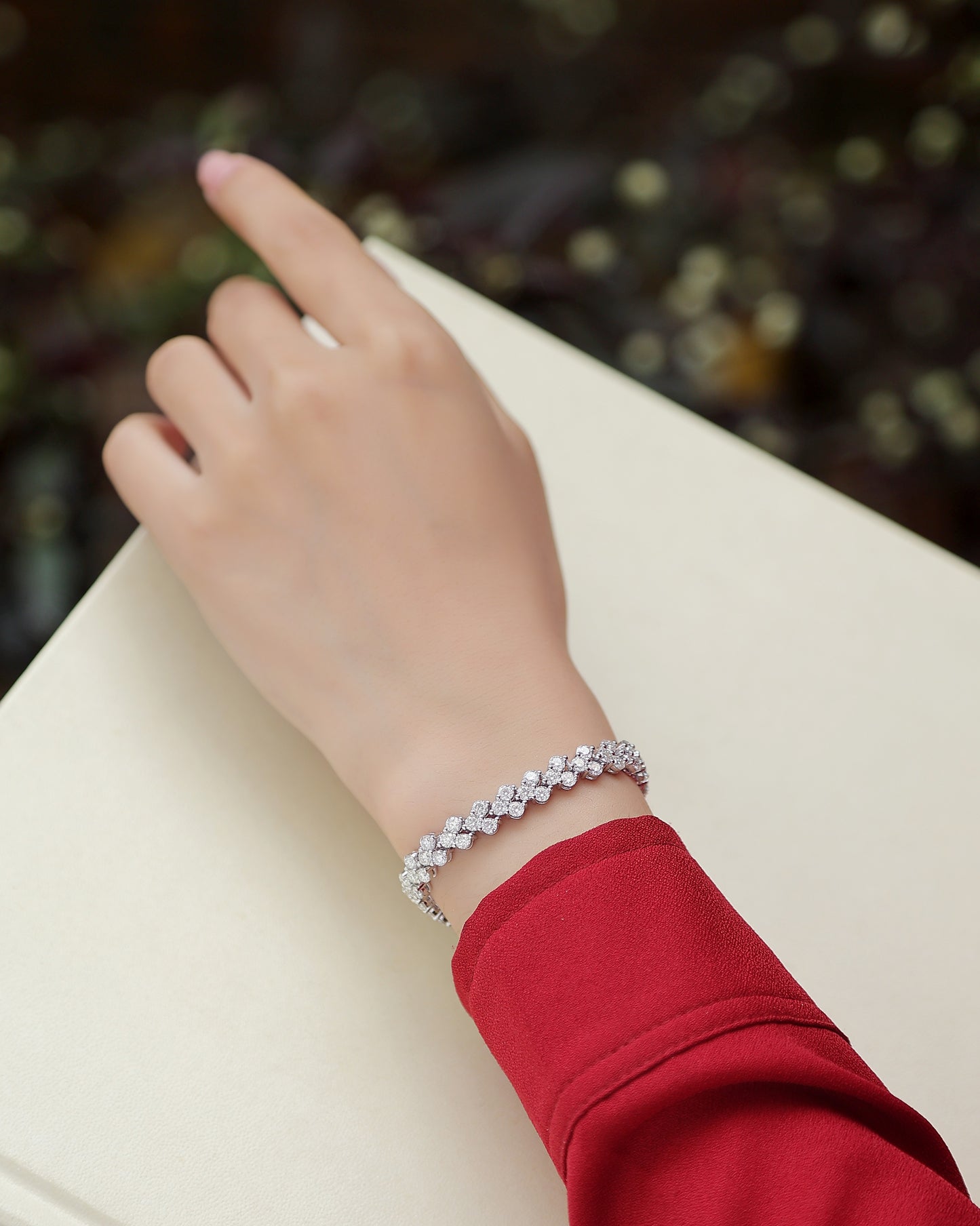 A hand wearing a Luminara moissanite cluster tennis bracelet in S925 sterling silver luxury wrist jewelry by MerchLuxx on a blurred background
