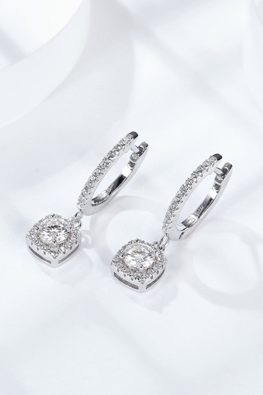 Pair of moissanite huggie drop earrings in sterling silver on a white background