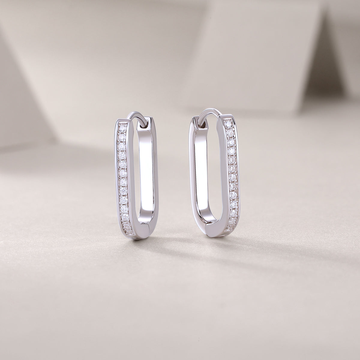 Avelisse pavé moissanite elongated huggie hoop earrings in platinum-plated sterling silver by MerchLuxx  on a light background