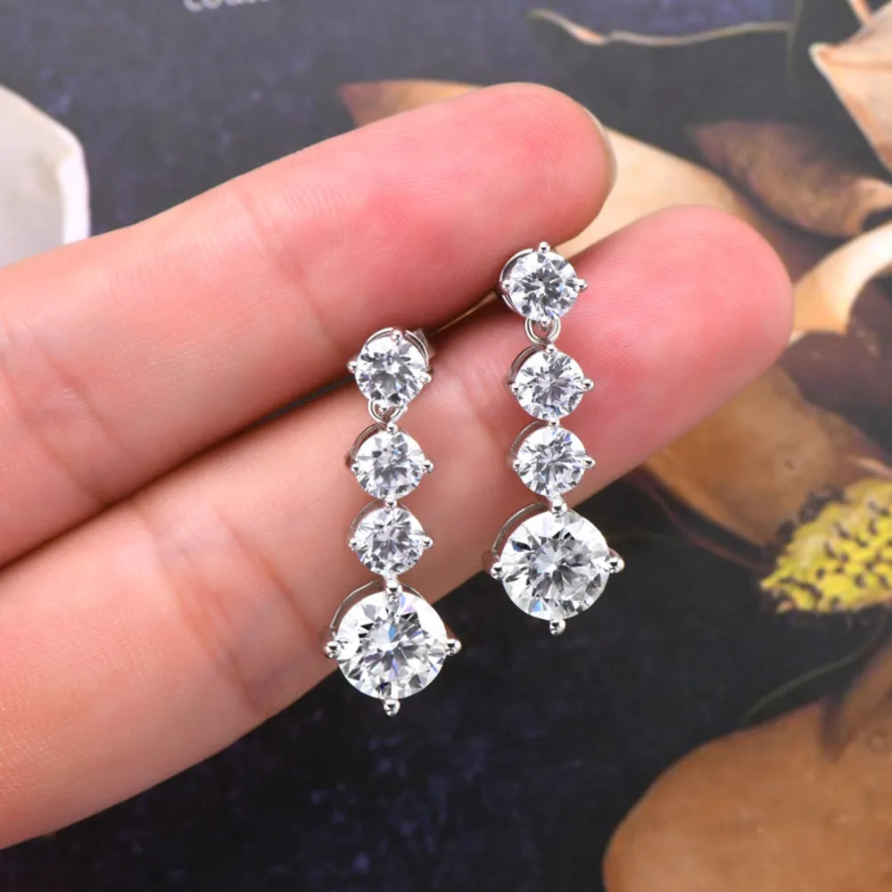 Hand holding Celestia™ three-stone moissanite drop earrings
