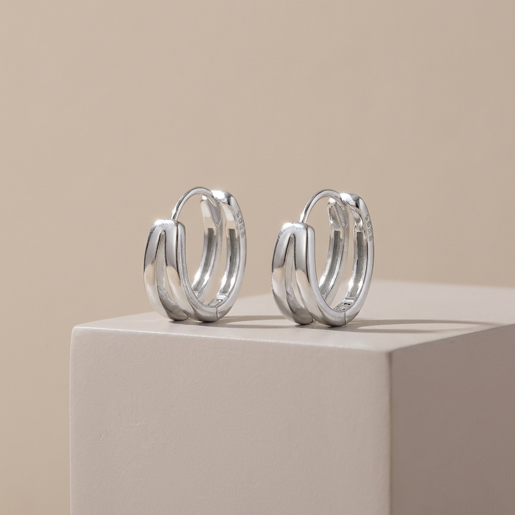 Pair of 925 sterling silver zircon huggie earrings with subtle sparkle  on a beige surface with a beige background