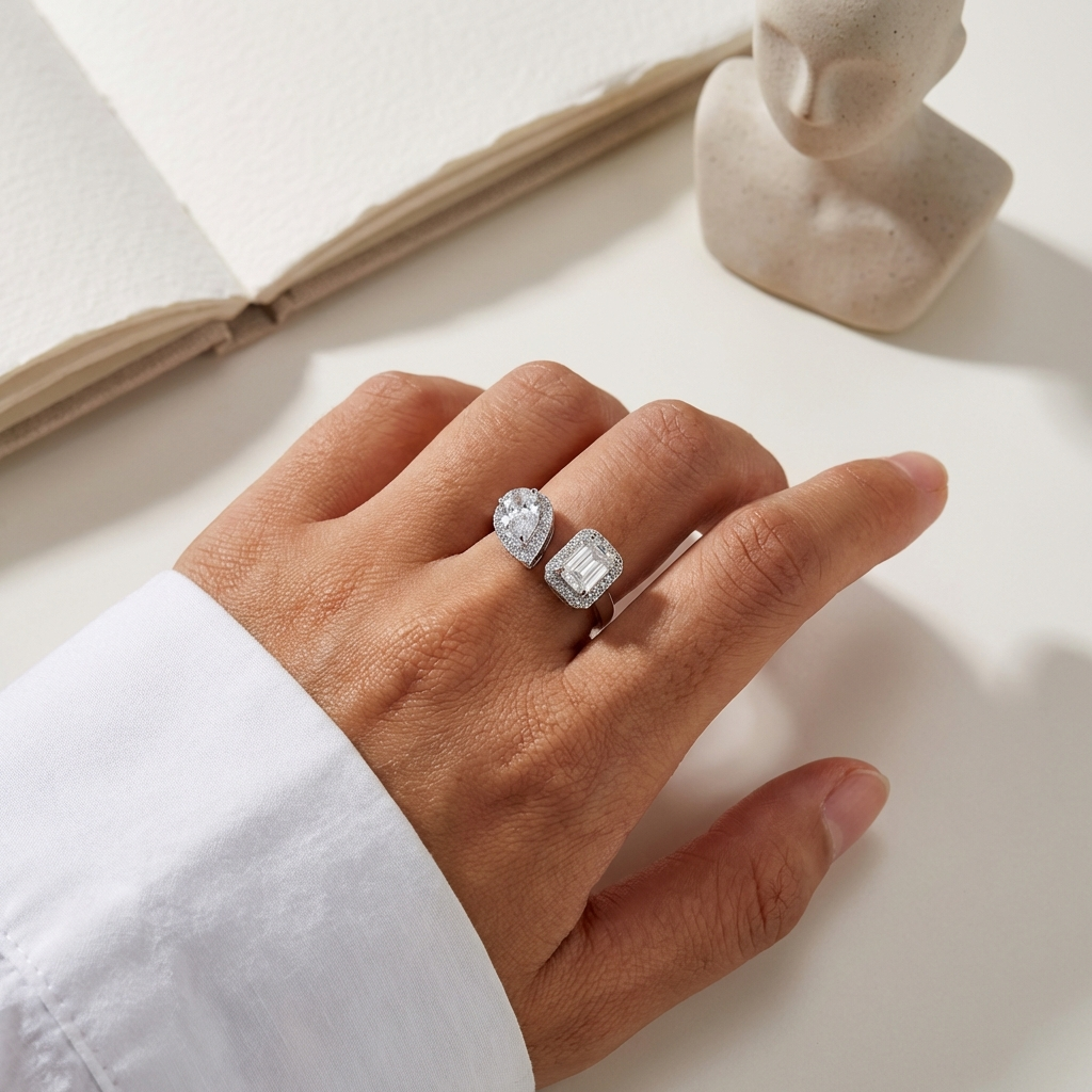 Hand wearing an emerald-cut moissanite open bypass ring with a pear accent stone in platinum-plated sterling silver on a neutral background