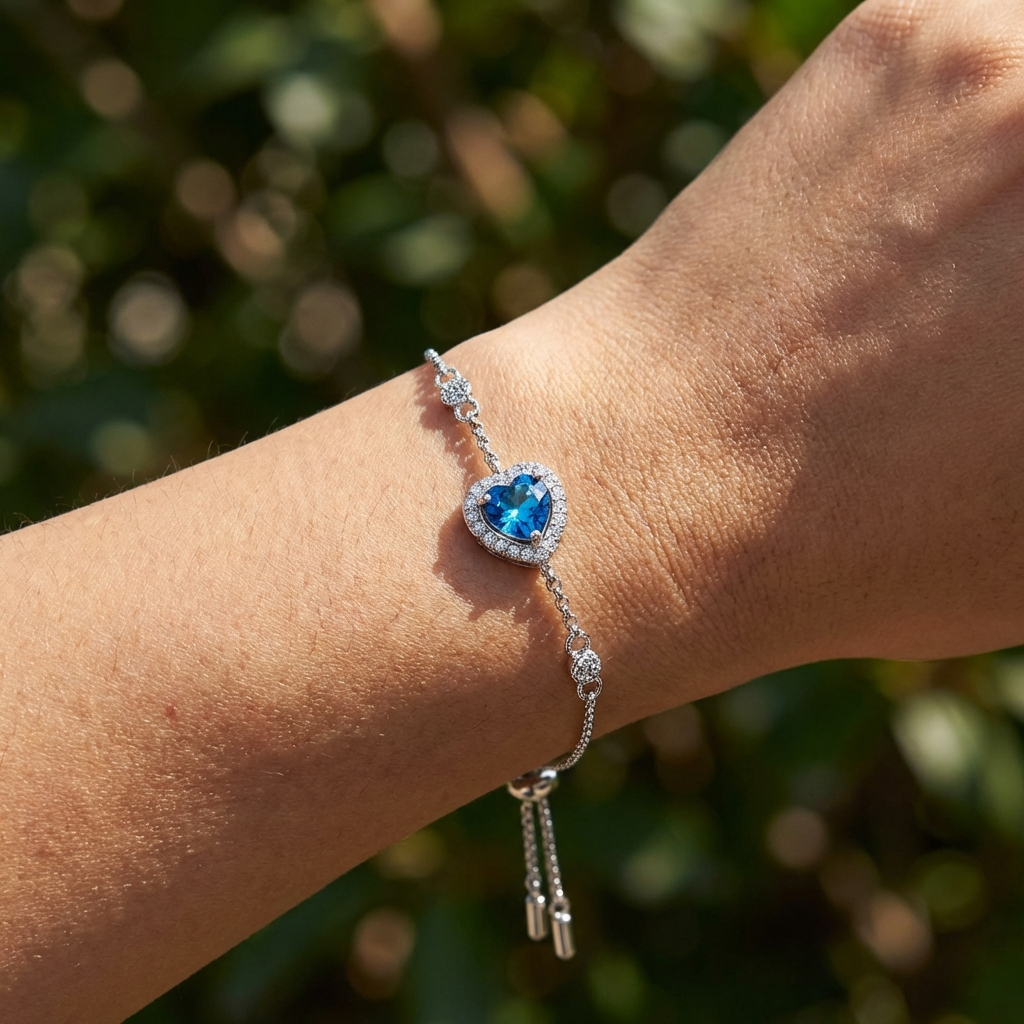 A Celestara blue moissanite heart bracelet in platinum-plated sterling silver with heart accents by MerchLuxxon against a blurred green background