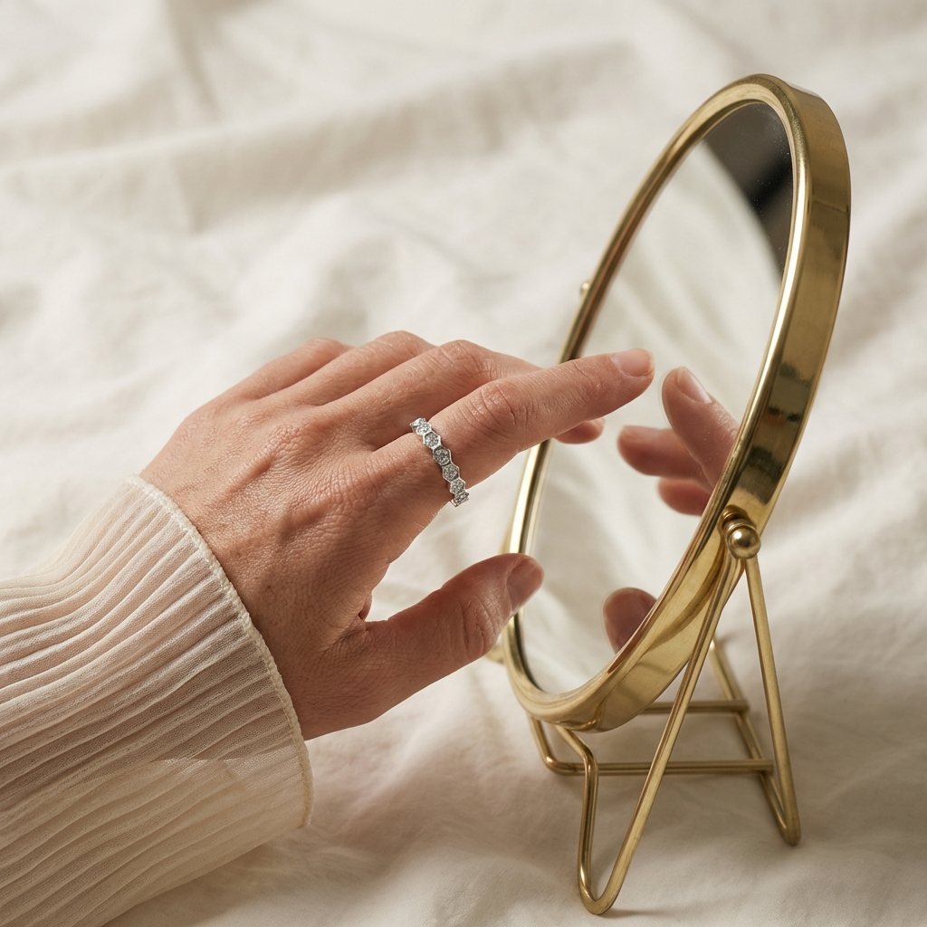 Gold-framed mirror on a white surface with a woman's hand touching it, wearing the Eternyx moissanite hexagon eternity ring in rhodium-plated sterling silver by MerchLuxx
