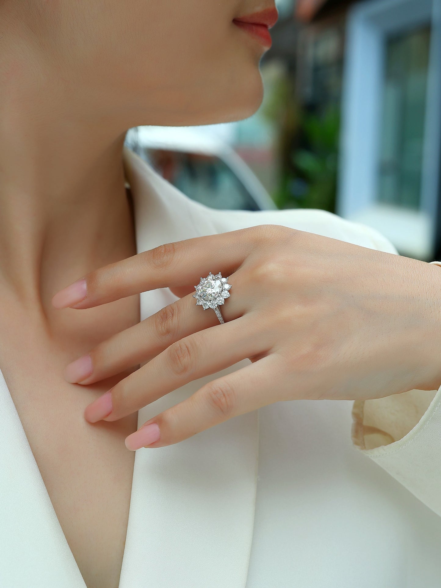 Close-up of a hand wearing a Soléa 3 carat moissanite floral halo ring in platinum-plated sterling silver statement engagement ring by MerchLuxxwith a blurred background