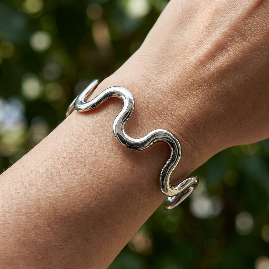 High polish stainless steel sculpted wave cuff bracelet with minimalist open design on a wrist with a blurred green background