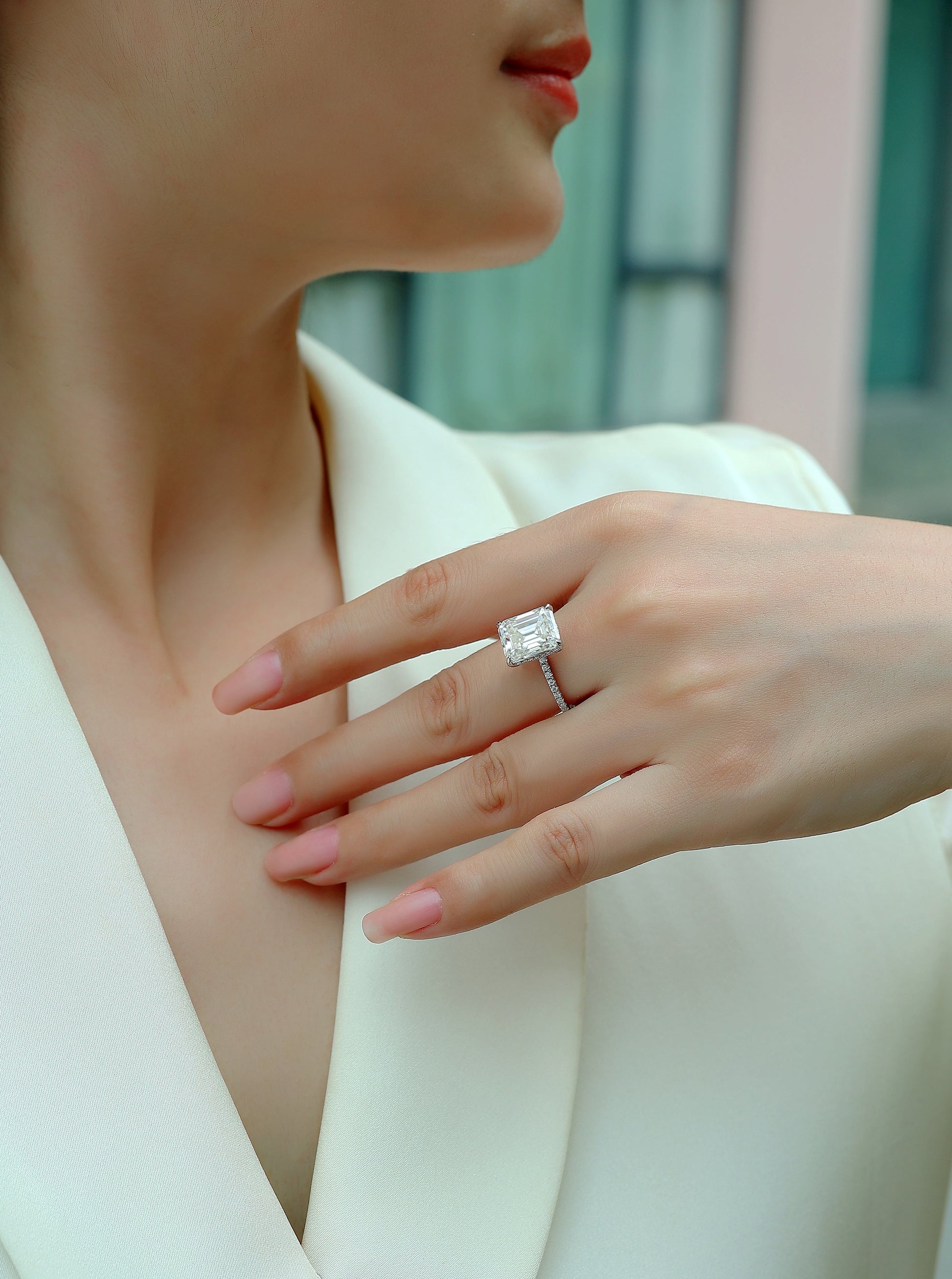 Close-up of a hand wearing  the Luminara 9x11mm octagonal moissanite engagement ring in platinum-plated sterling silver cathedral setting by Merchluxx with a blurred background