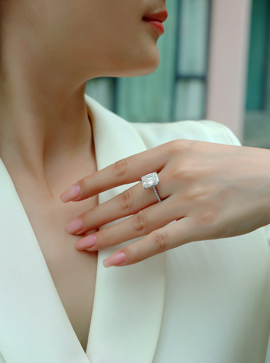 Close-up of a hand wearing  the Luminara 9x11mm octagonal moissanite engagement ring in platinum-plated sterling silver cathedral setting by Merchluxx with a blurred background