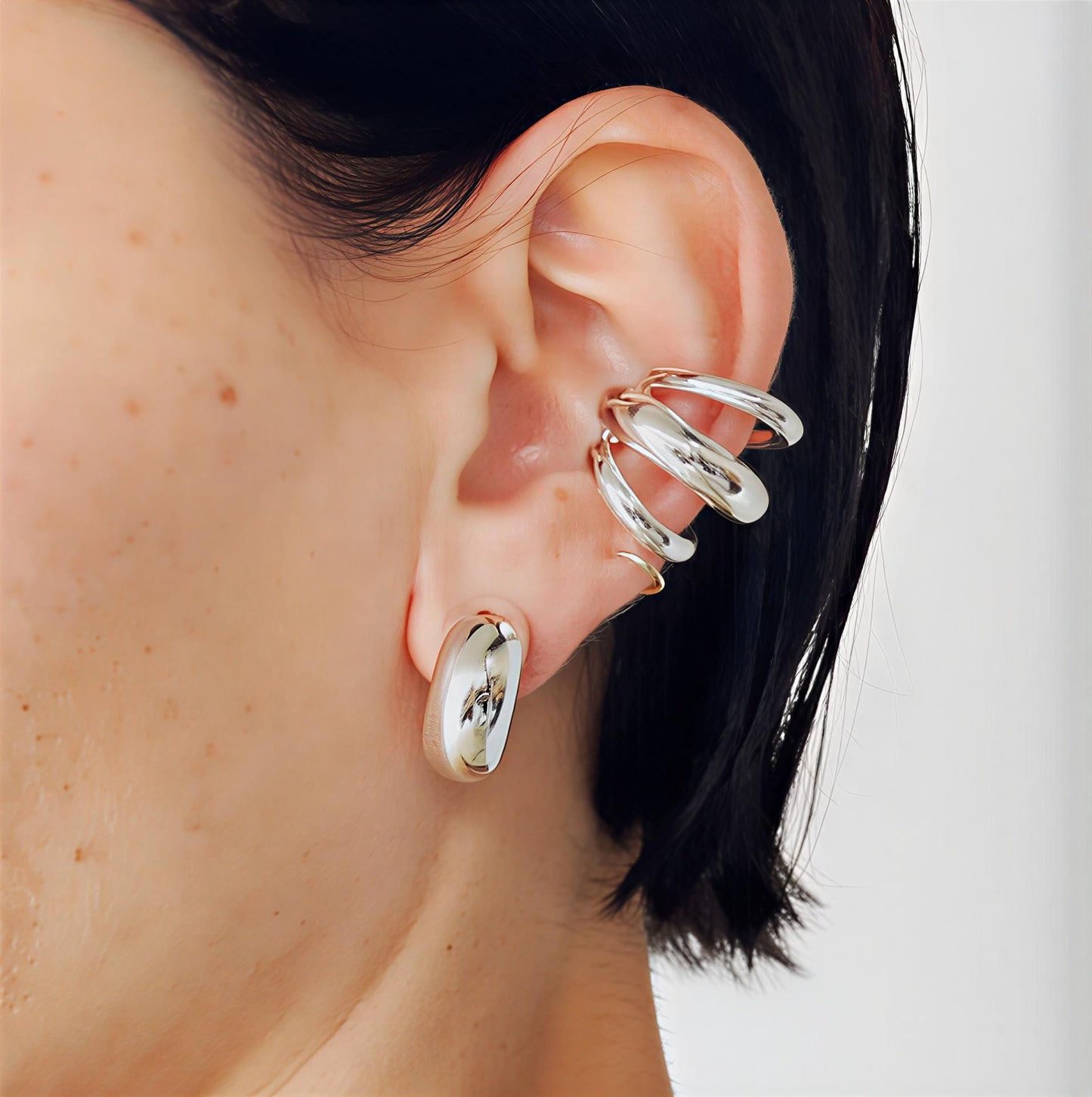 Sculpted layered stainless steel cuff earrings with polished silver-tone finish on a person's ear with a neutral background