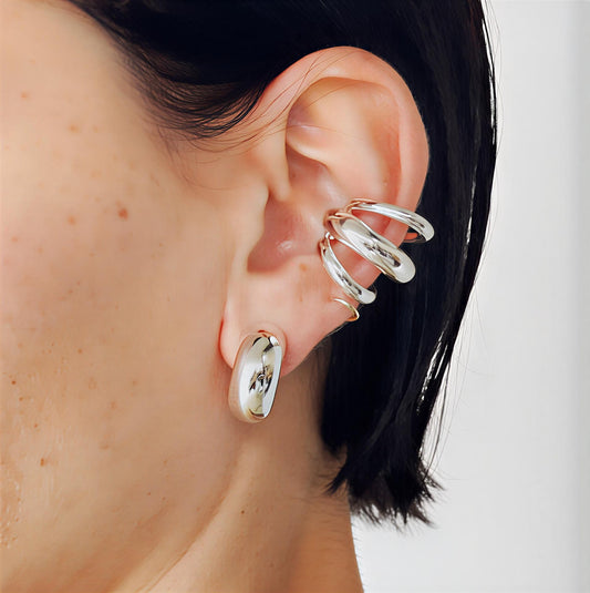 Sculpted layered stainless steel cuff earrings with polished silver-tone finish on a person's ear with a neutral background