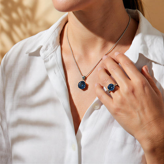 Person wearing Astrielle 10-carat blue moissanite ring and pendant necklace set in sterling silver by MerchLuxx set against a neutral background
