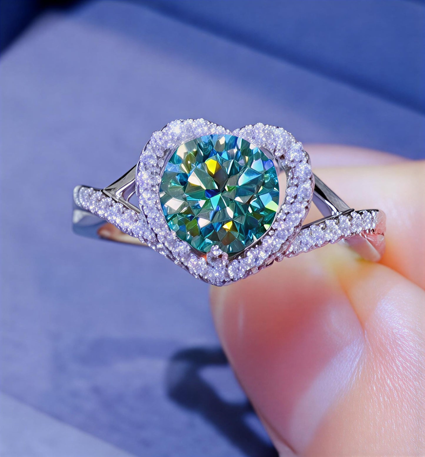  1-carat heart moissanite halo ring in platinum-plated sterling silver available in green, yellow, and white, held between fingers against a blue background