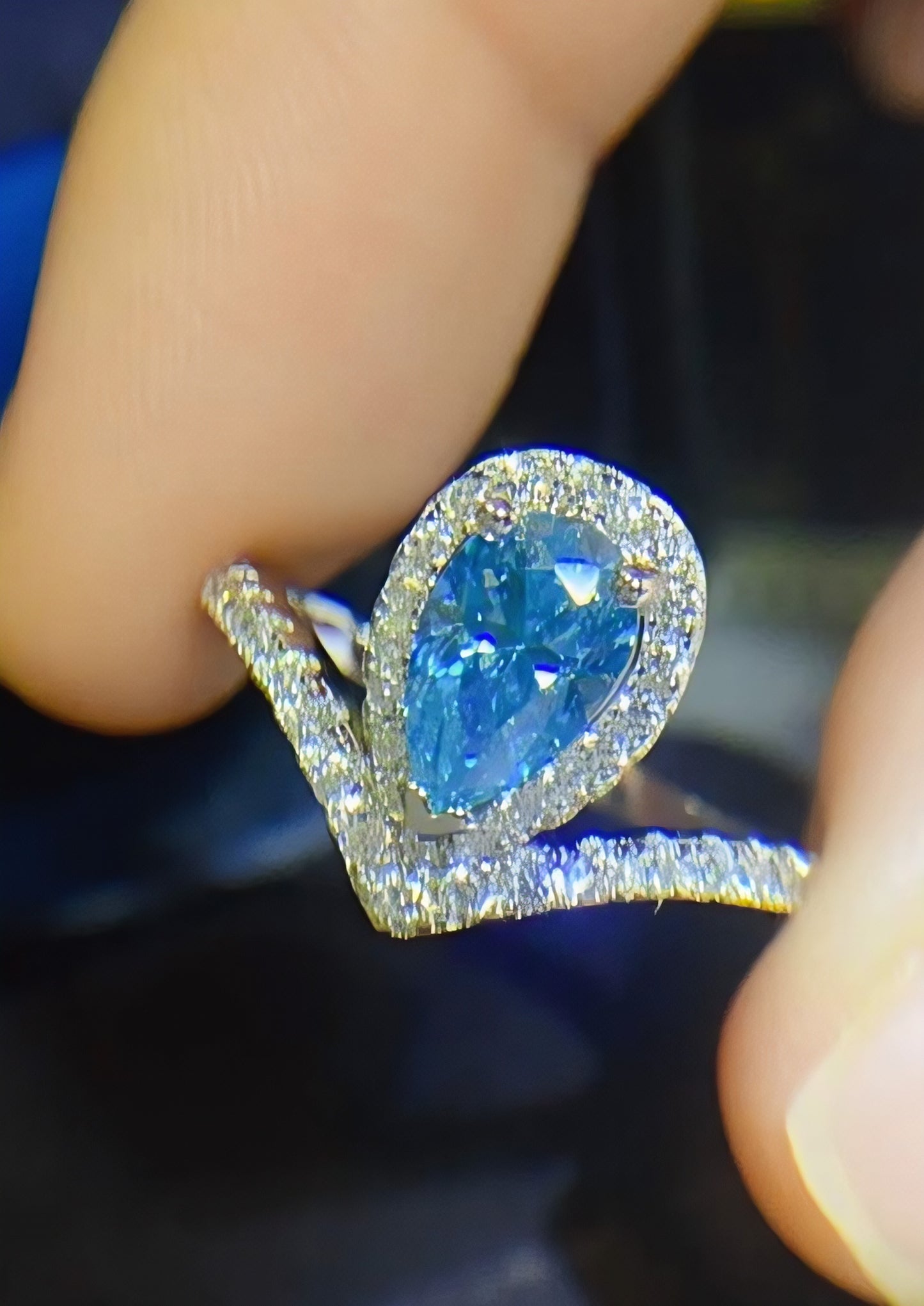 Amouria 1-carat pear-shaped moissanite heart halo ring in platinum-plated sterling silver by MerchLuxx held between two fingers against a blurred background