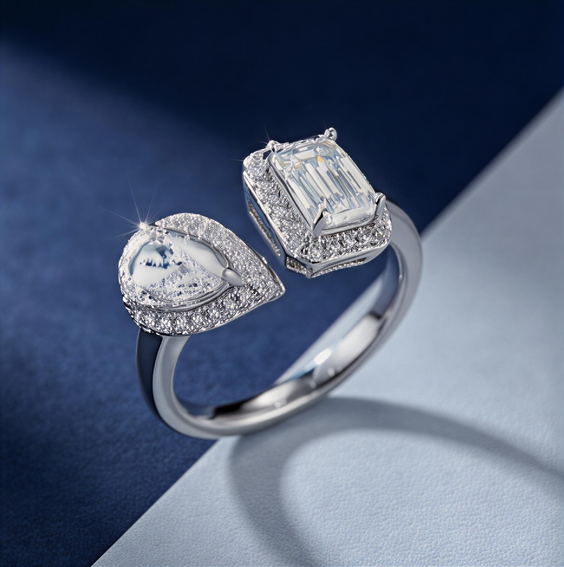 emerald-cut moissanite open bypass ring with pear accent stone in platinum-plated sterling silver on a blue and gray gradient background